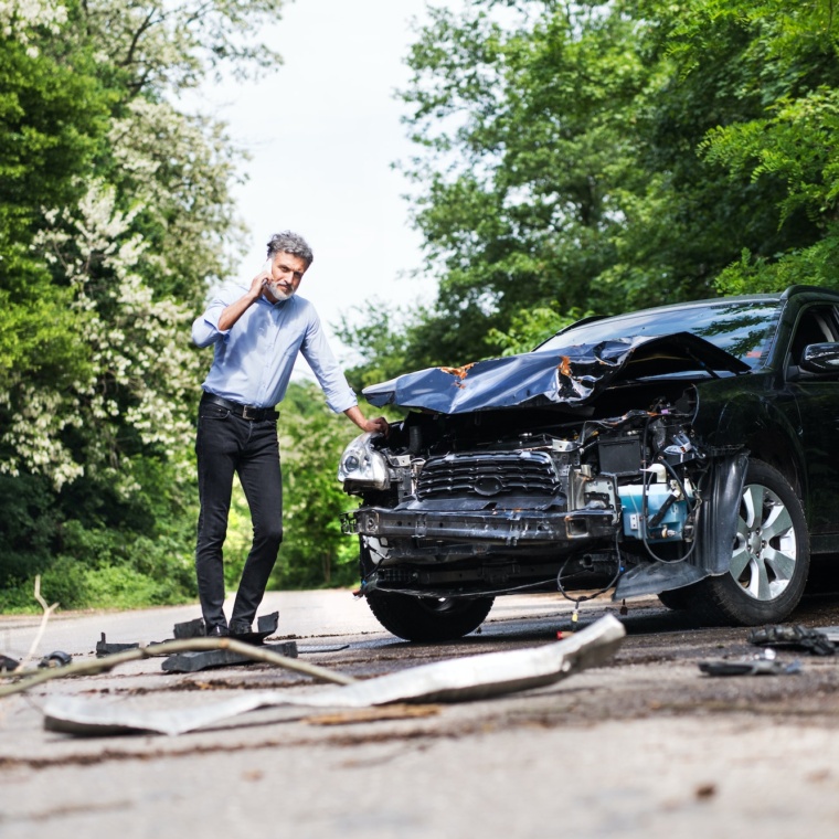 Mature man standing by the car, making a phone call after a car accident.