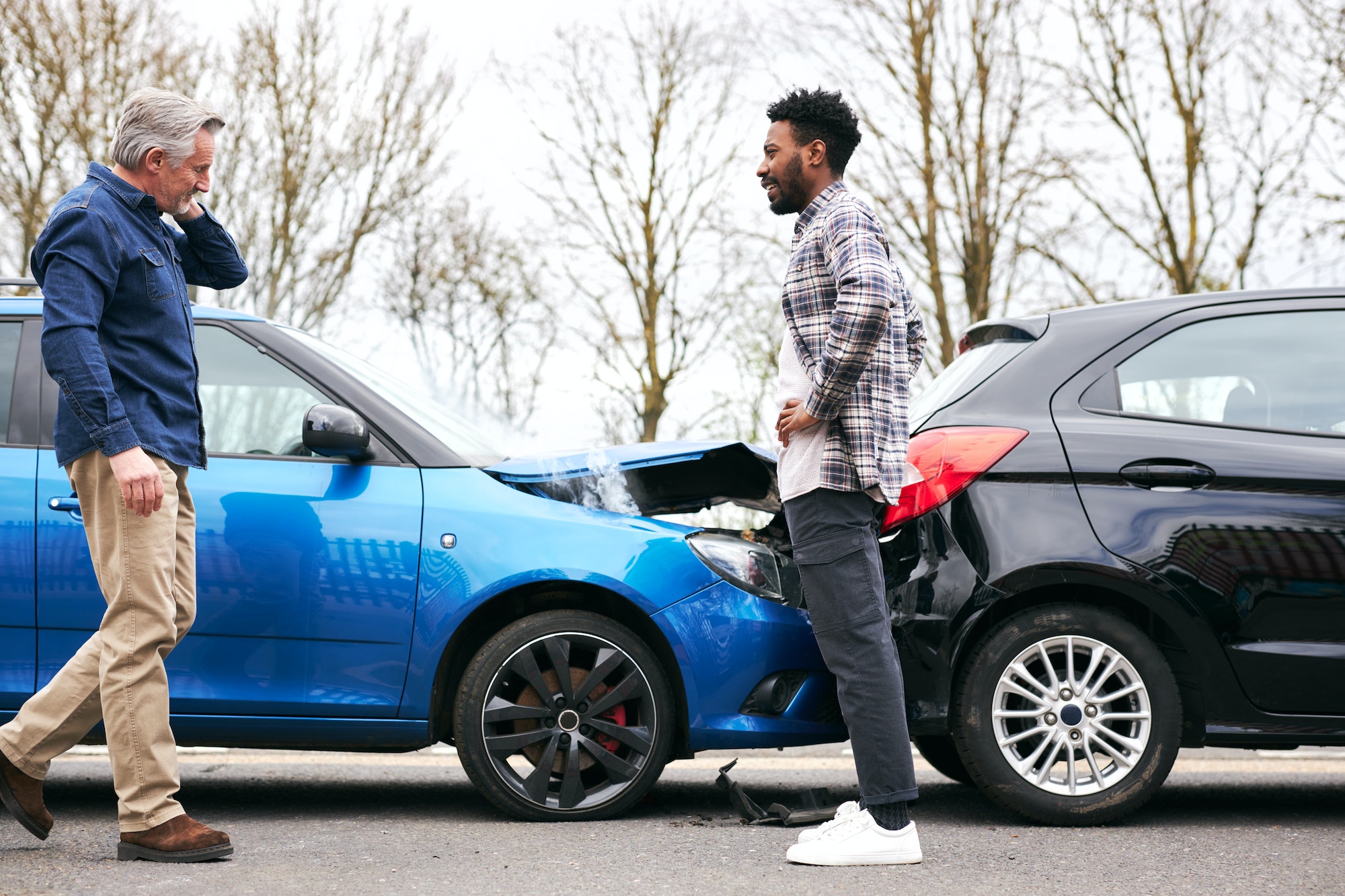 Senior Male And Younger Male Drivers Get Out Of Cars And Inspect Damage After Traffic Accident