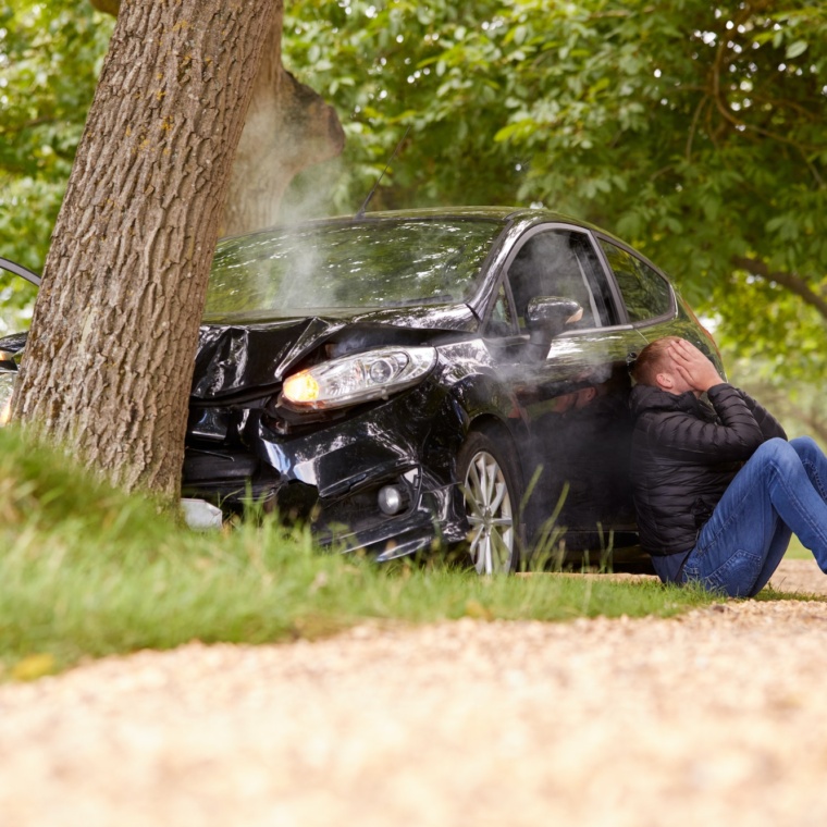 Teenage Driver With Head In Hands Sitting Next To Wrecked Car After Crashing Into Tree