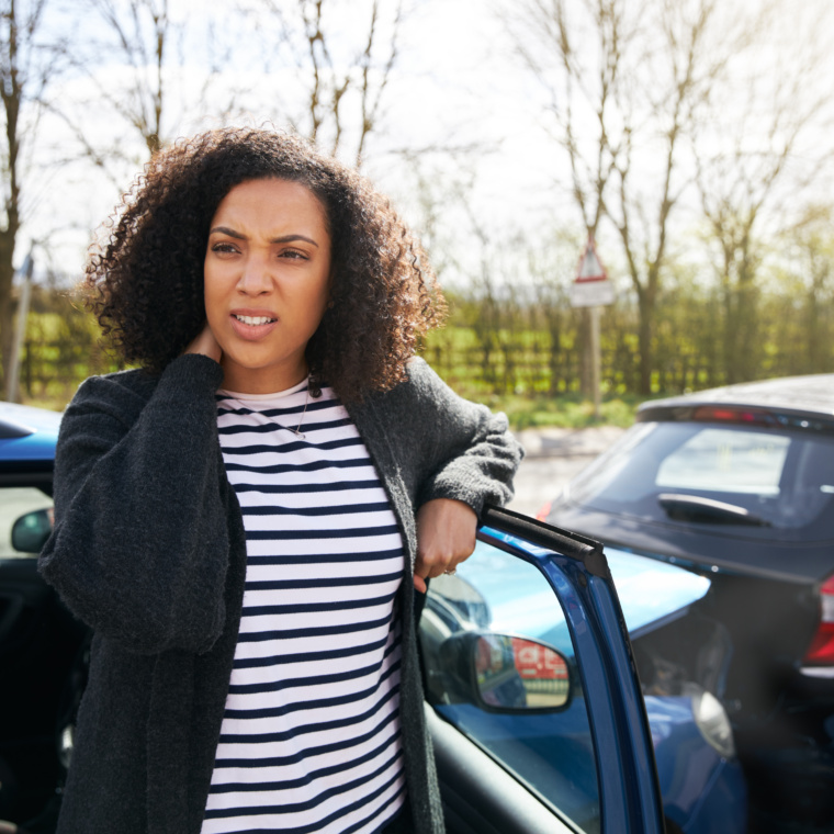 Female Driver With Whiplash Injury Standing By Damaged Car After Road Traffic Accident