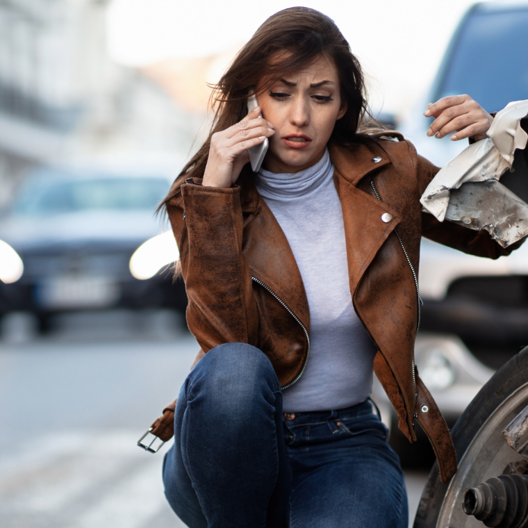 Young sad woman talking on mobile phone next to her wrecked car.