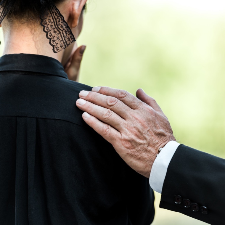 cropped view of elderly man touching woman on funeral