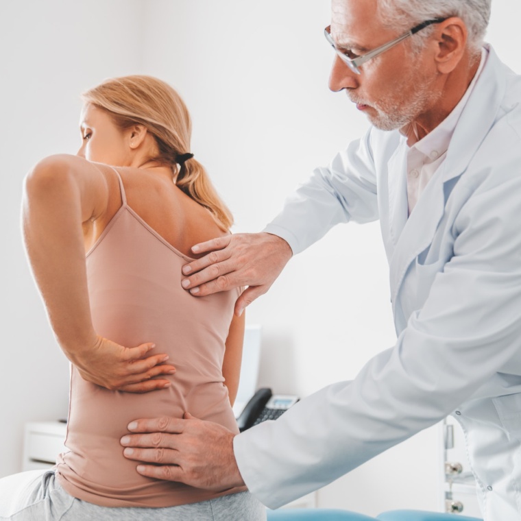 Senior male orthopedist examining patient's back in clinic