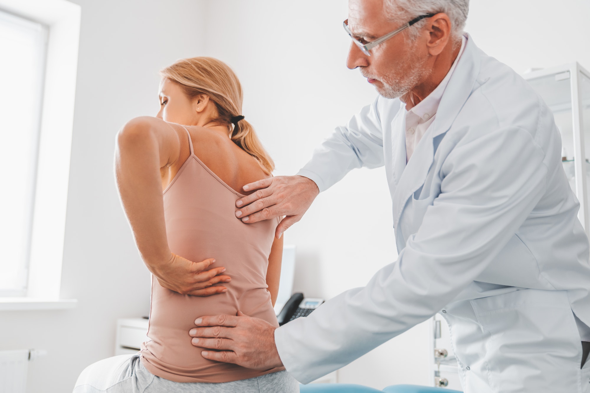 Senior male orthopedist examining patient's back in clinic